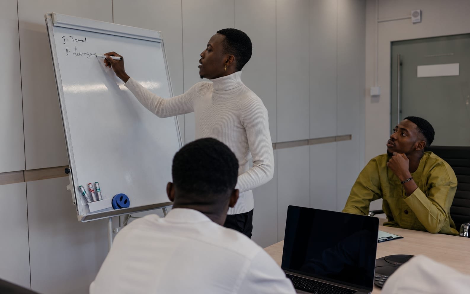 A presenter writing a numbered list of points on a whiteboard in a team meeting